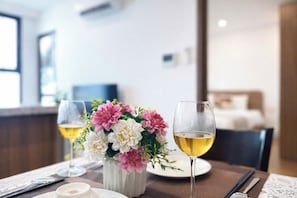 A hotel room with a dining table set for two, featuring a vase of flowers and two glasses of white wine. - Vinhomes D'capitale - Kim's House (Hanoi)