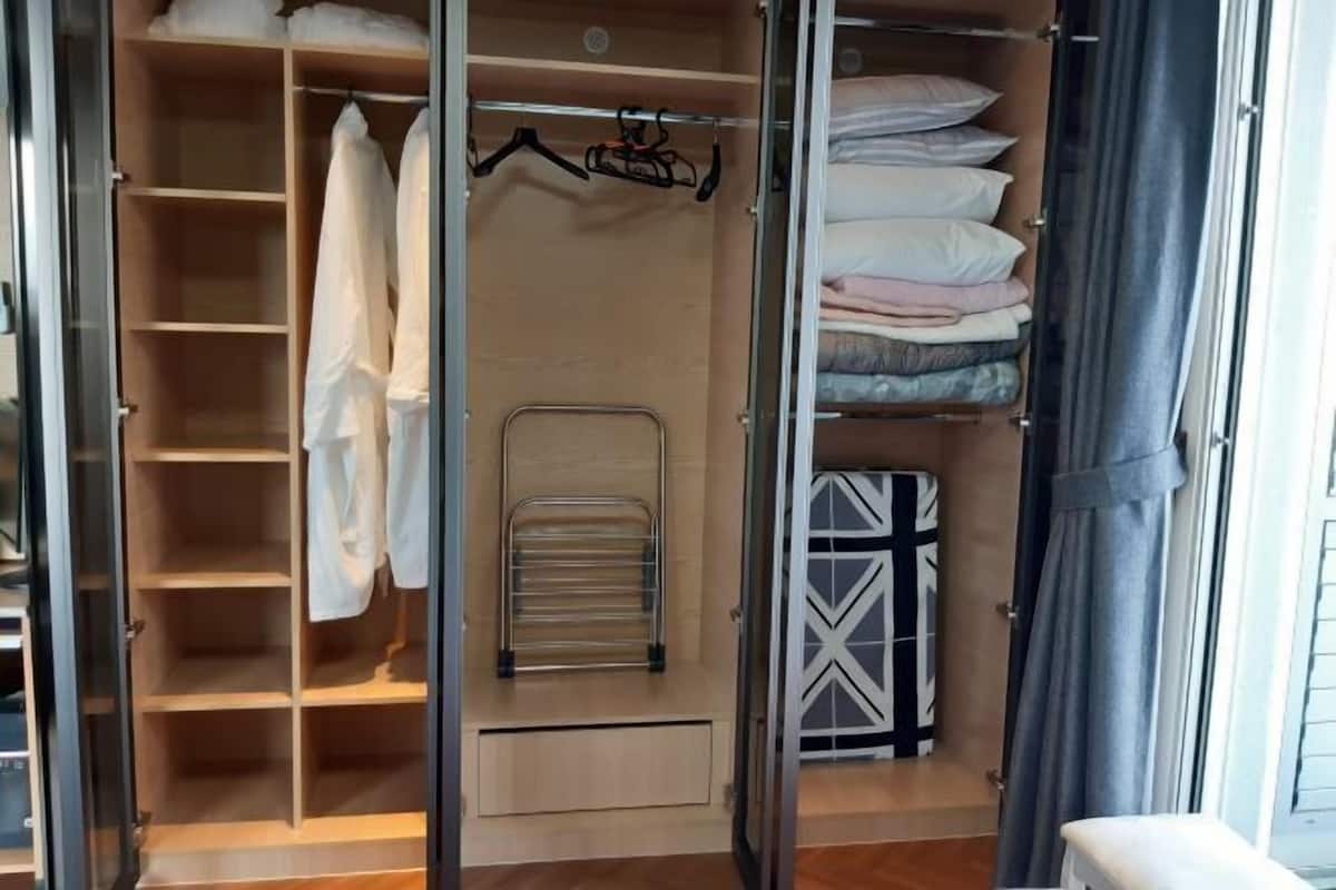 A walk-in closet with open doors, featuring shelves, a hanging rack, and folded bedding.