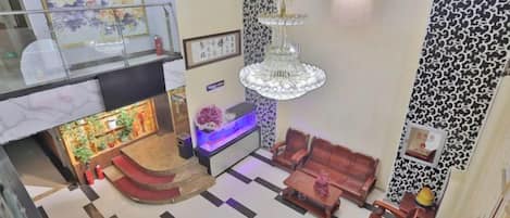 A hotel lobby with a reception desk, seating area, staircase, and a chandelier.