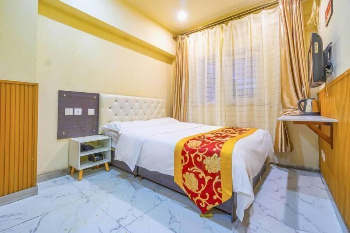 Une chambre d’hôtel avec un lit, une petite table de chevet, un téléviseur fixé au mur et une fenêtre avec des rideaux.