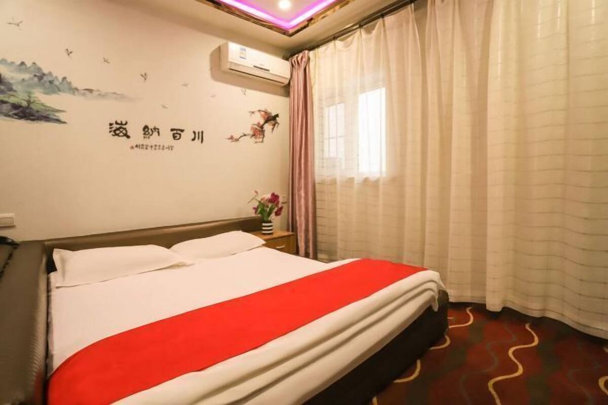 Une chambre d’hôtel avec un lit, des rideaux, un mur décoré d’œuvres d’art et un appareil de climatisation.