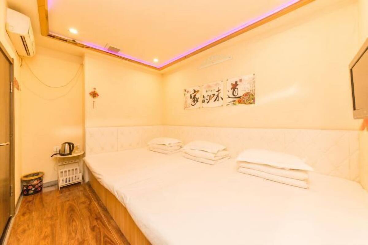 Une chambre d’hôtel avec un lit, une petite table avec une bouilloire, un téléviseur fixé au mur et un luminaire au plafond.