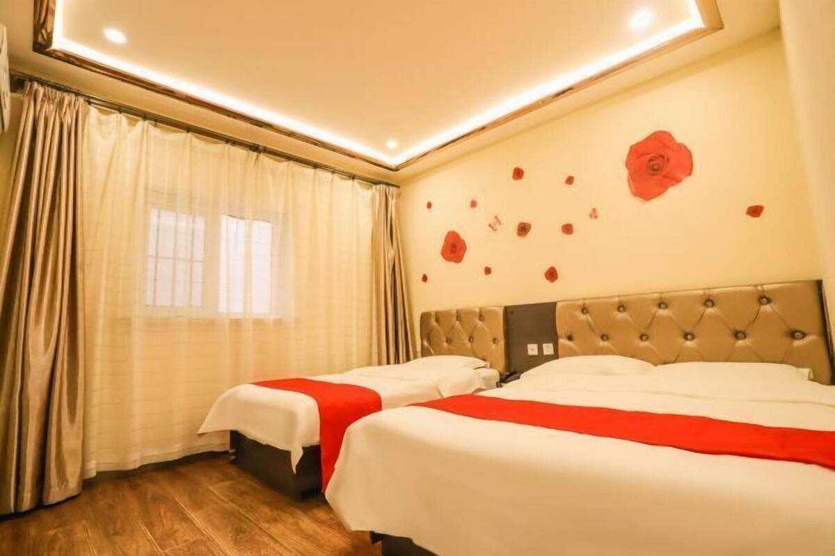 Une chambre d’hôtel avec deux lits, une grande fenêtre avec des rideaux et un mur décoré de motifs floraux rouges.