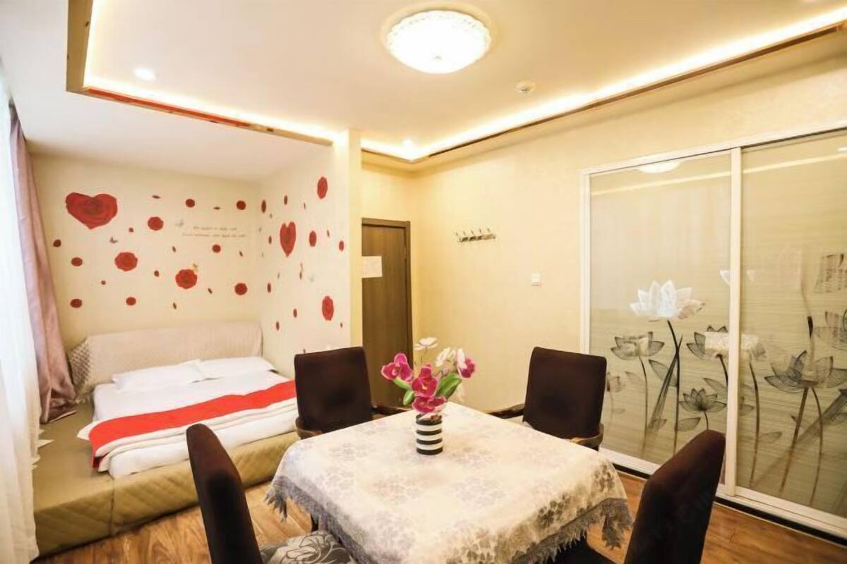 Une chambre d’hôtel avec un lit, une table à manger avec des chaises, un vase avec des fleurs et un mur décoré de motifs en forme de cœur.