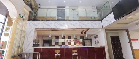 A hotel lobby with a marble reception desk, two bar stools, a glass railing, and a flat-screen TV.