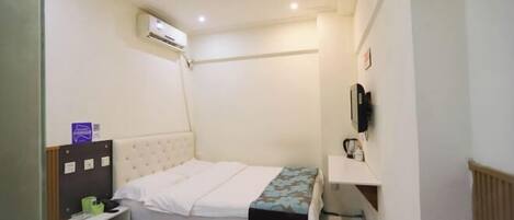 A small, compact room with a bed, a bedside table, a wall-mounted TV, and an air conditioning unit.