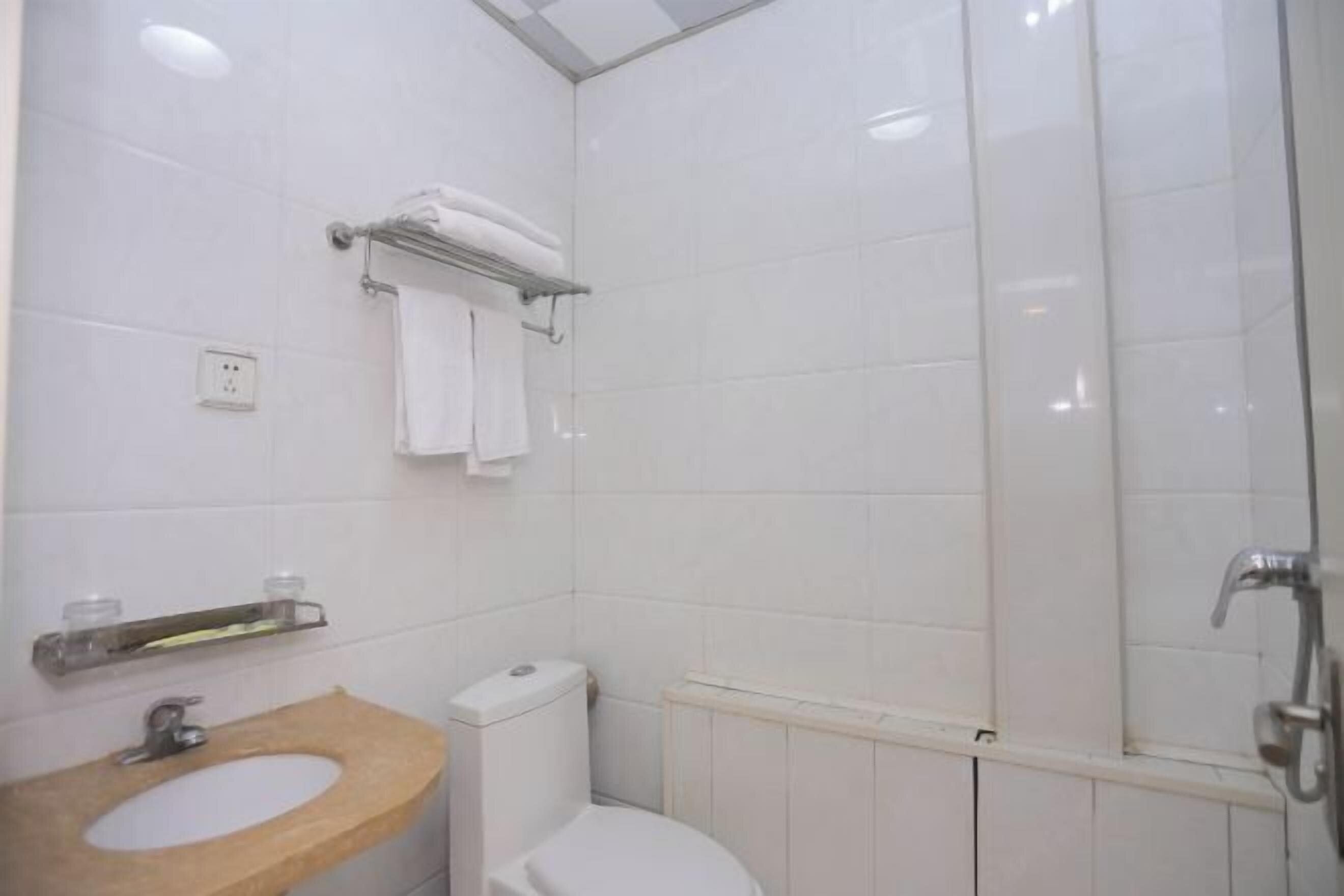 Een badkamer met een houten wastafelmeubel, toilet, handdoekhouder en douchehoek.