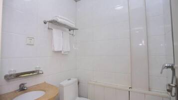 Een badkamer met een houten wastafelmeubel, toilet, handdoekhouder en douchehoek.