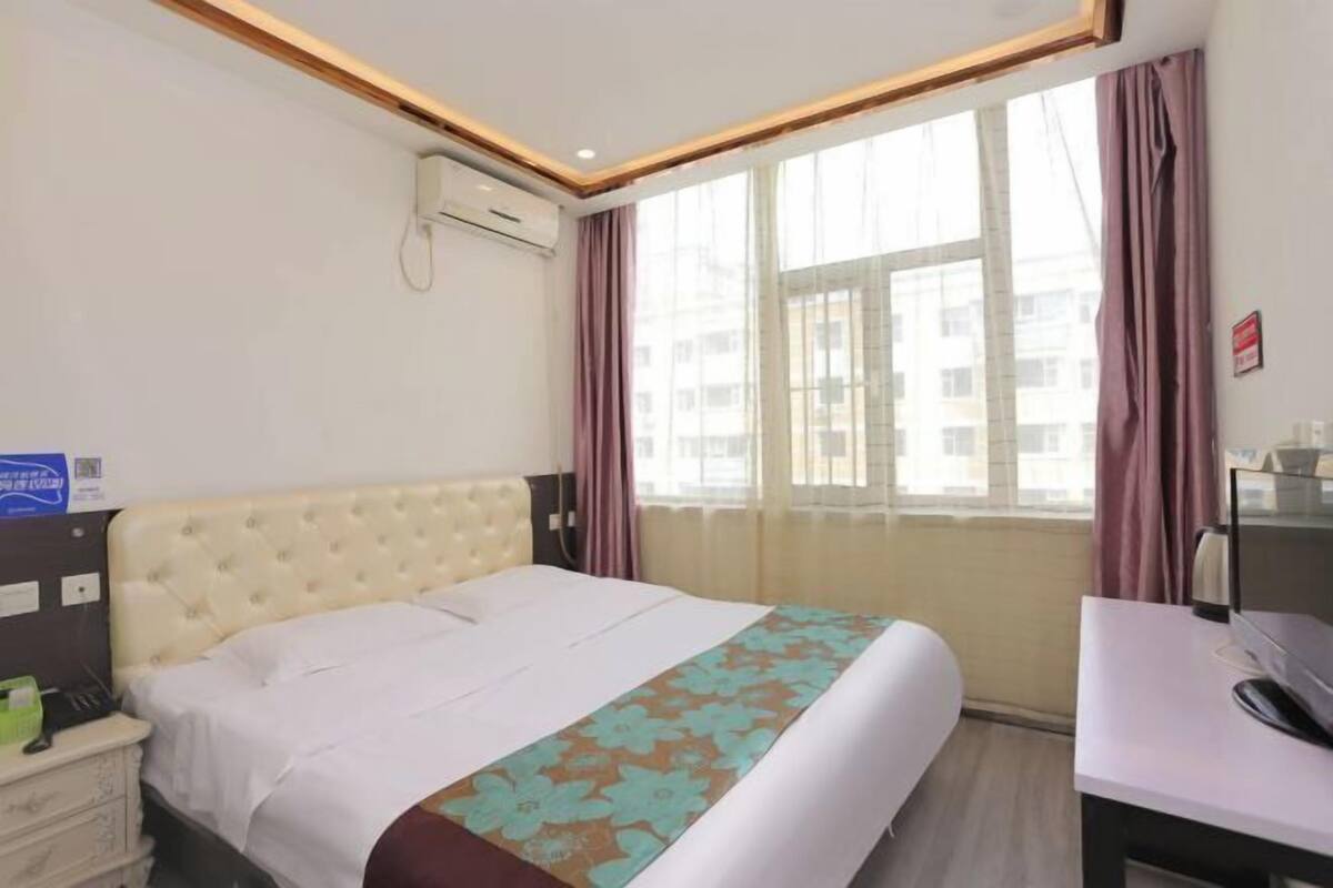 Une chambre d’hôtel équipée d’un lit, d’un bureau, d’une chaise, d’un appareil de climatisation et d’une fenêtre avec des rideaux.