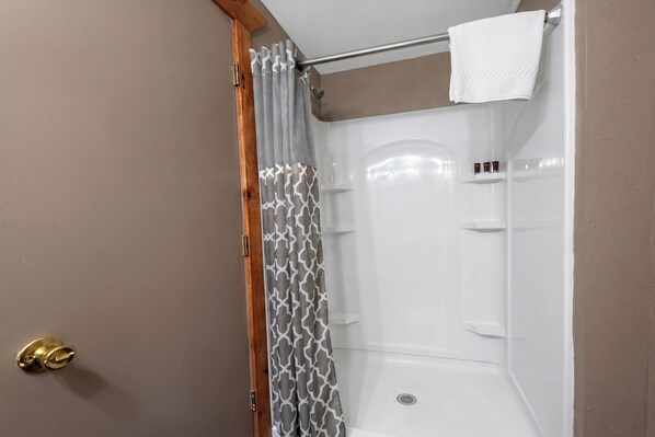 A shower with a white curtain, a towel hanging on a rod, and a door with a brass handle.