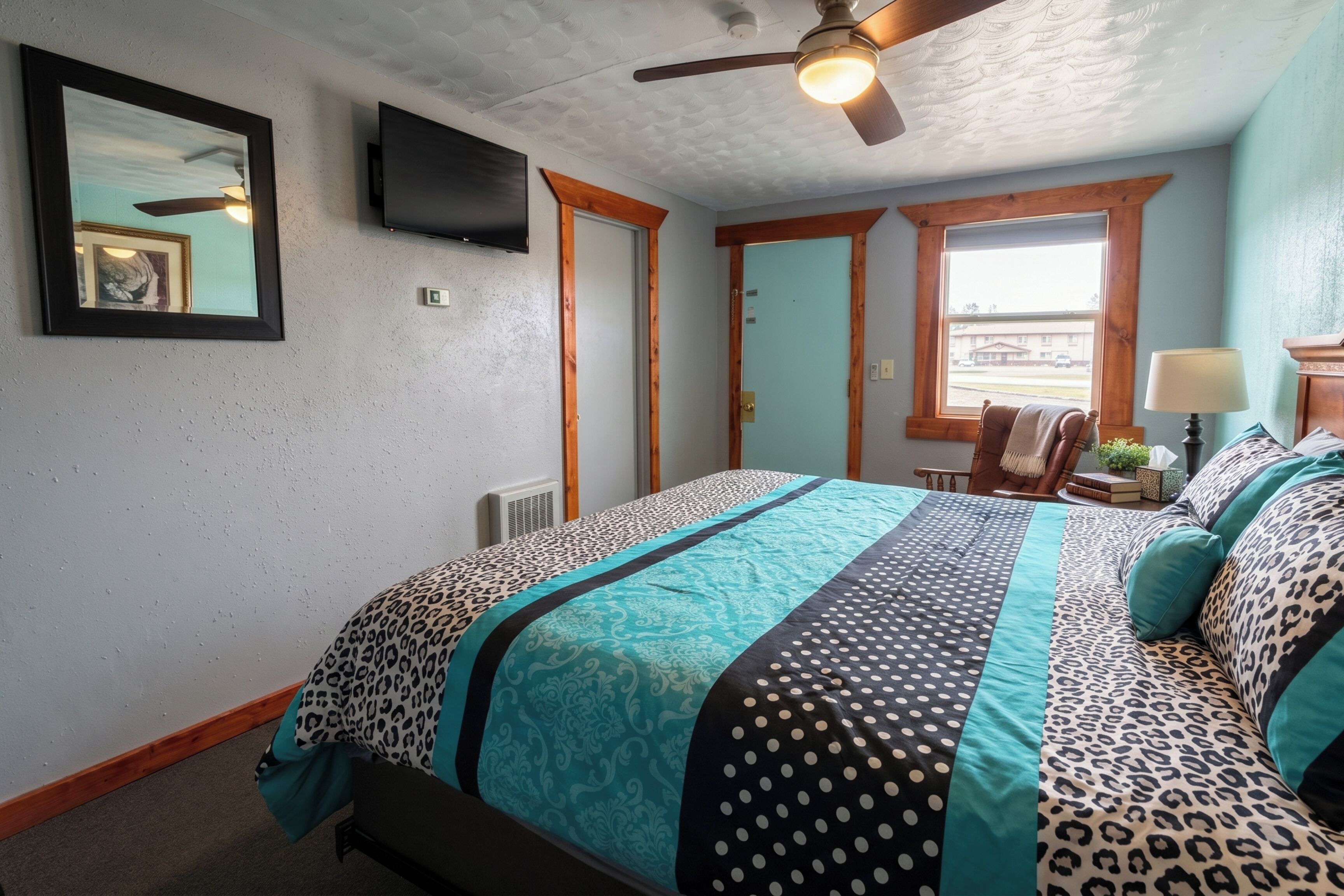 Un dormitorio con cama, ventilador de techo, televisor y ventana con vistas.