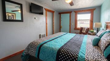 Un dormitorio con cama, ventilador de techo, televisor y ventana con vistas.