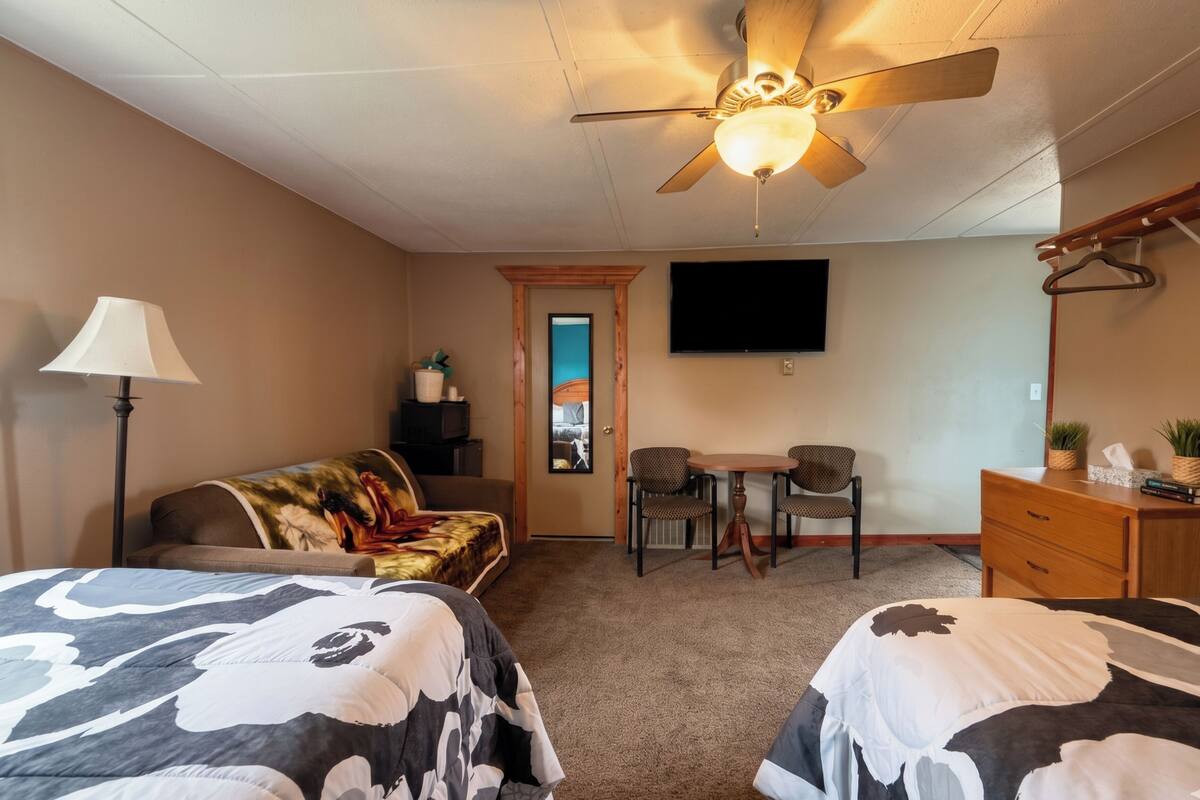 A bedroom with two beds, a ceiling fan, a TV, a desk, and a chair.