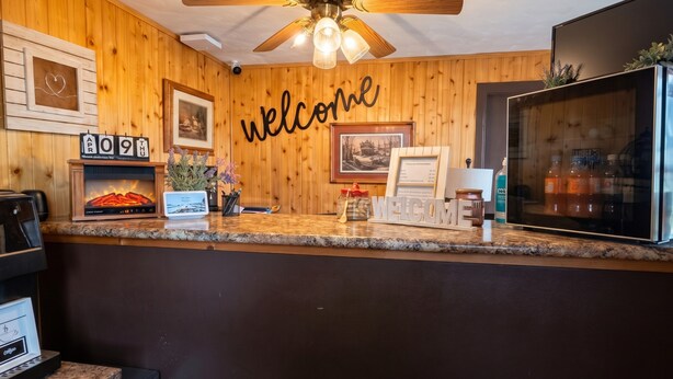 A wooden interior with a 'welcome' sign, a ceiling fan, a framed picture, and a refrigerator. - KJ's Inn and Suites By OYO Gettysburg U.S. Hwy 212 (Gettysburg)
