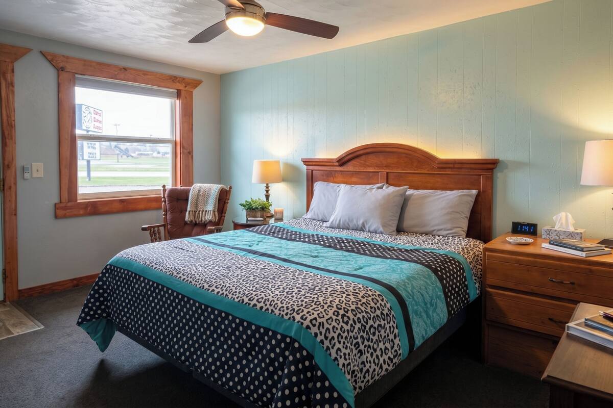 A bedroom with a bed, a nightstand, a chair, a window, and a ceiling fan.
