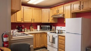 A kitchen with wooden cabinets, a microwave, a stove, a refrigerator, a sink, and a fire extinguisher. - KJ's Inn and Suites By OYO Gettysburg U.S. Hwy 212 (Gettysburg)