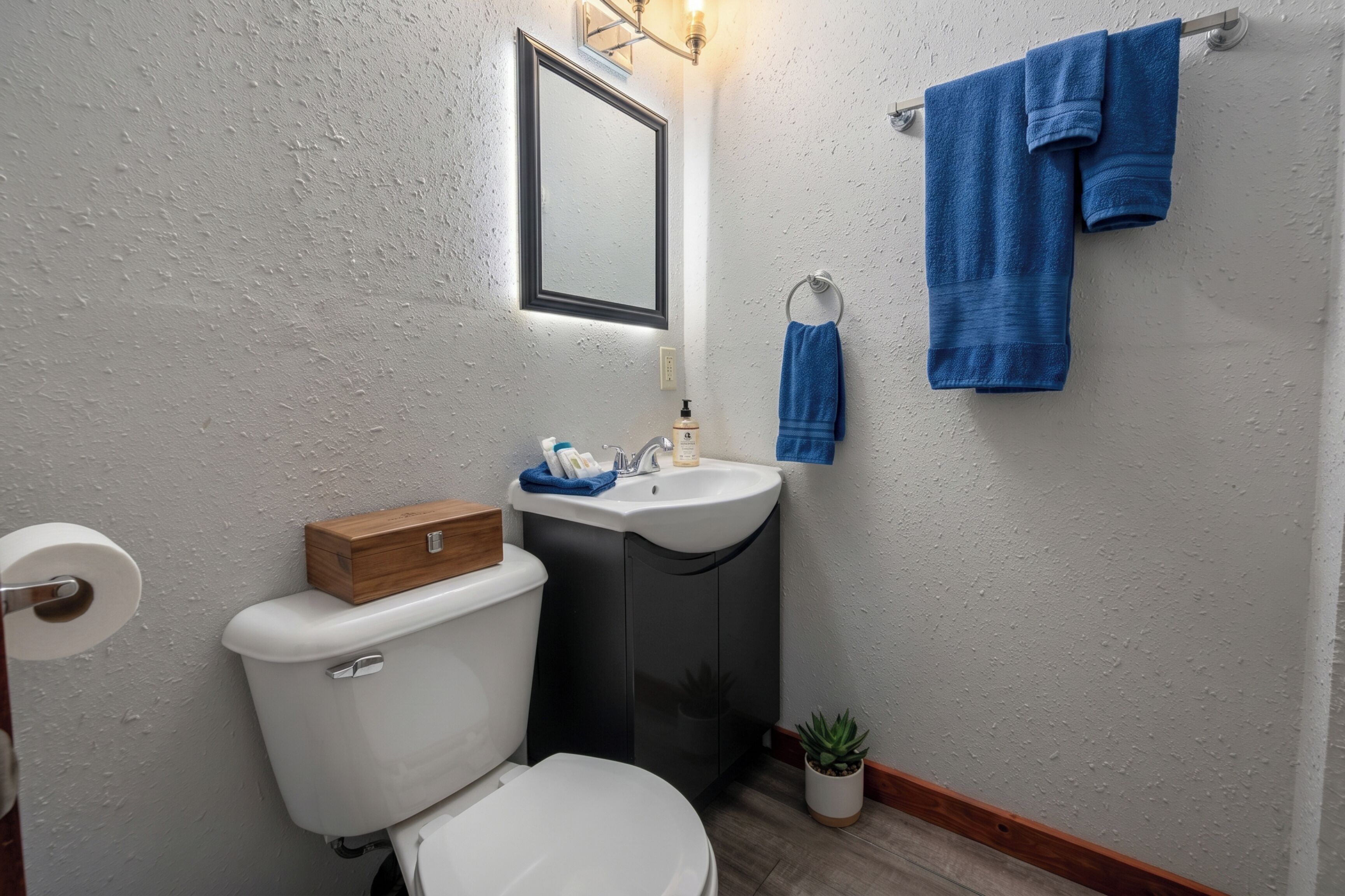 A bathroom with a toilet, sink, mirror, and blue towels.