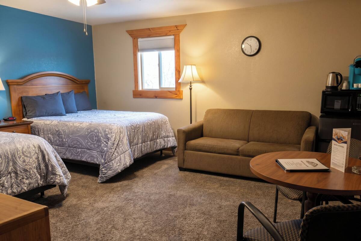 A bedroom with two beds, a sofa, a lamp, a clock, and a coffee maker.