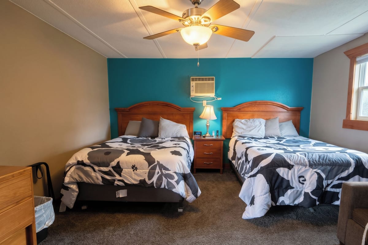 A bedroom with two beds, a ceiling fan, an air conditioning unit, and a bedside lamp.