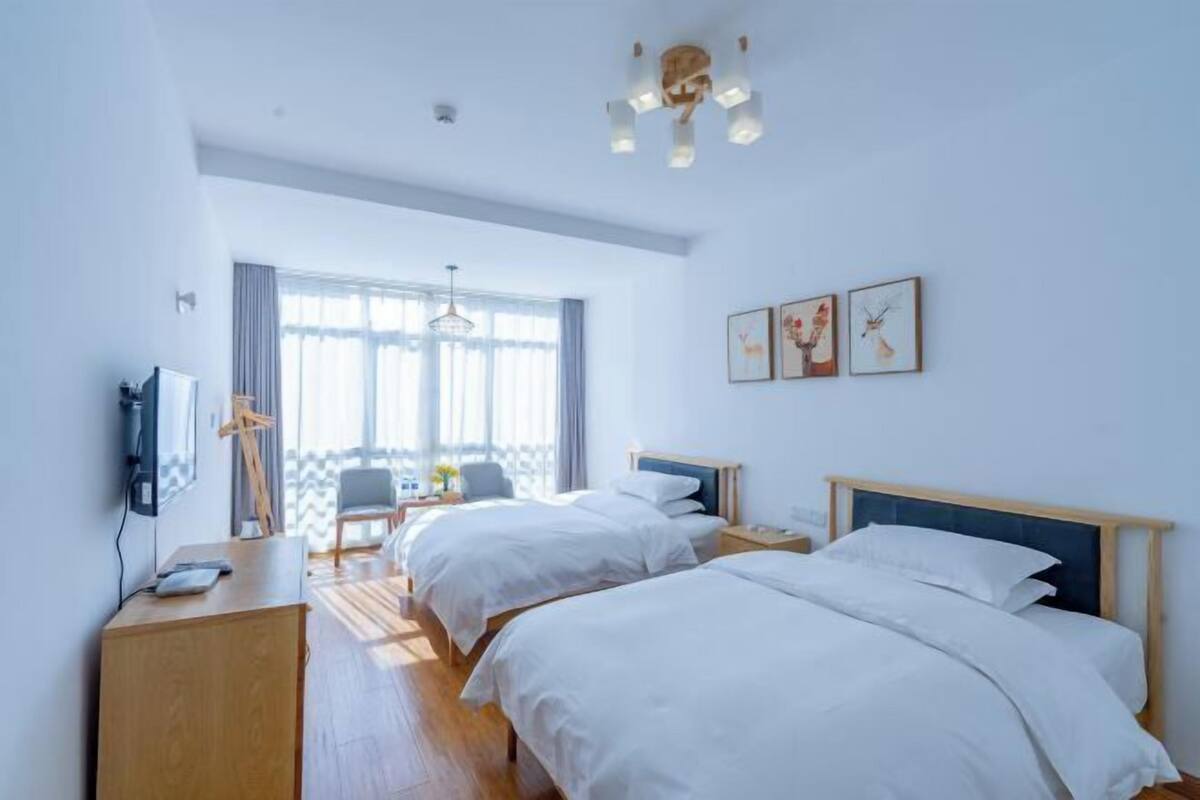A hotel room with two beds, a desk, a chair, a TV, and a balcony with a view.