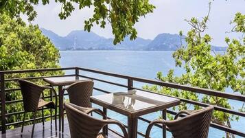 A terrace with wicker furniture and a glass table overlooking a lake with mountains in the background.