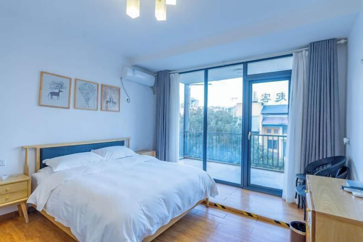 A hotel room with a bed, bedside table, and a view of a balcony.