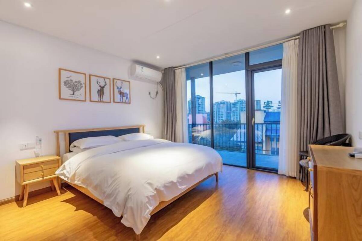 A bedroom with a bed, a nightstand, a desk, and a window with a city view.