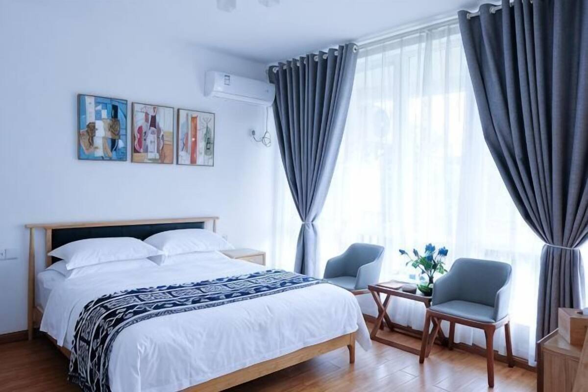A bedroom with a bed, two chairs, a small table, and a window with curtains.