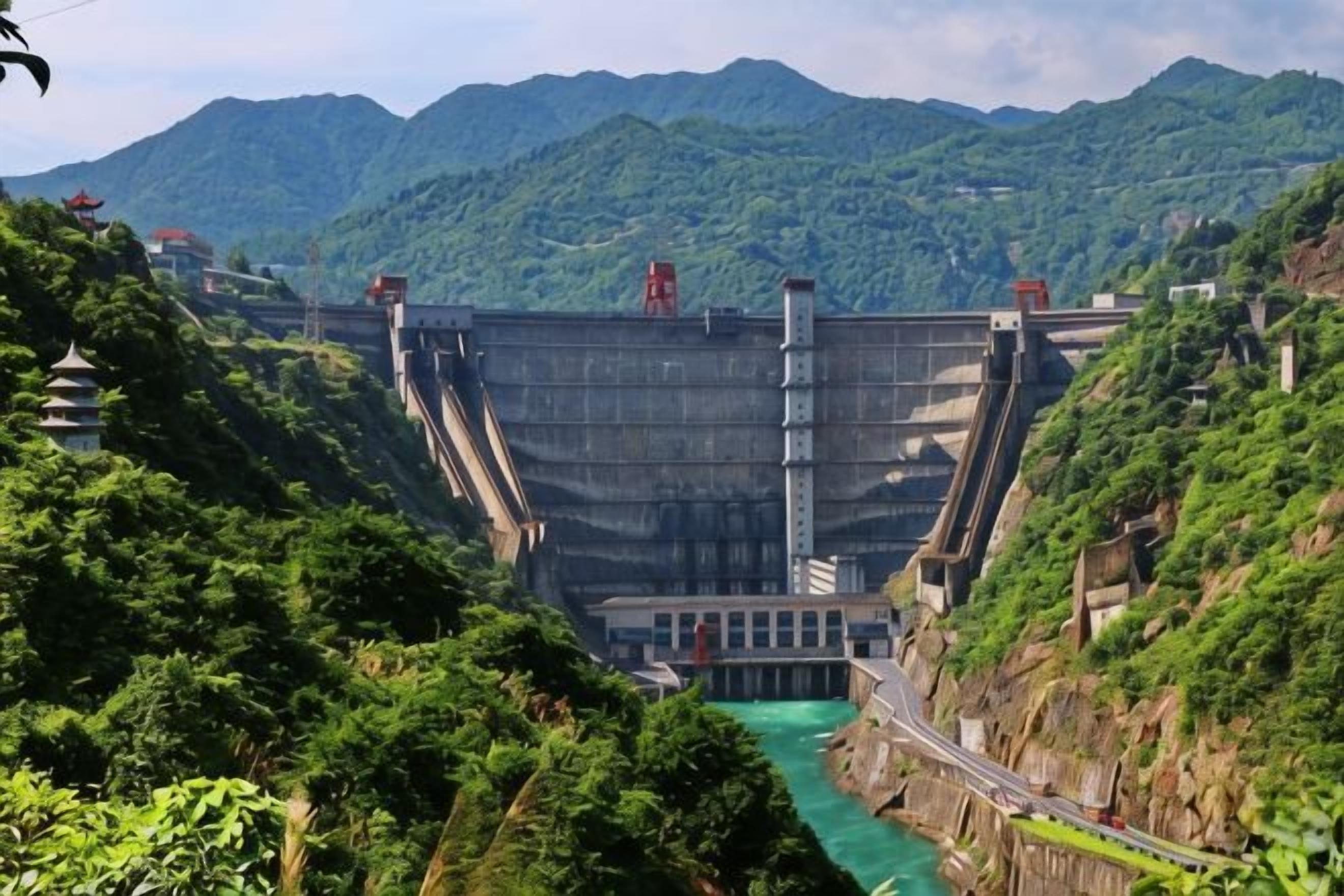 A large dam with a road leading to it, surrounded by lush greenery and mountains.