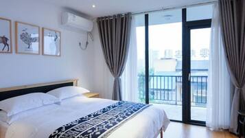 A bedroom with a bed, a window with curtains, a balcony, and framed pictures on the wall.