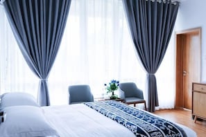 Una habitación de hotel con una cama, dos sillones, una mesita con un florero y un armario.