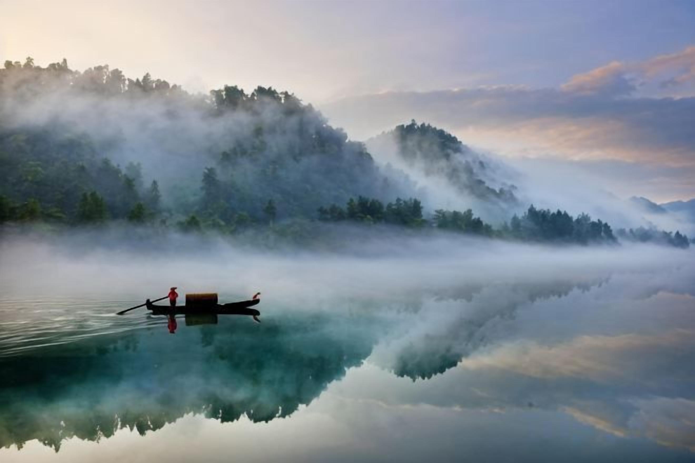 Un lago tranquilo con un bote, montañas cubiertas de niebla y un reflejo claro.