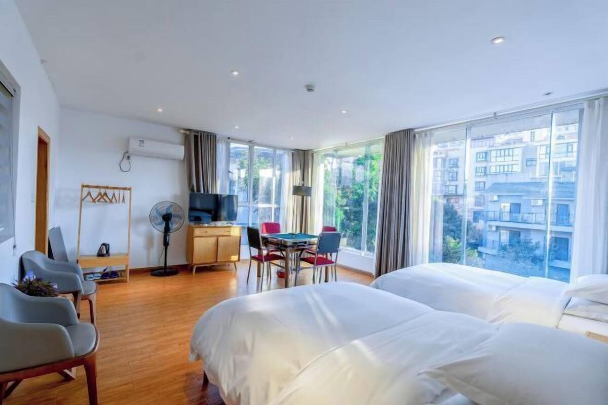 A hotel room with two beds, a desk, a TV, and a dining area.