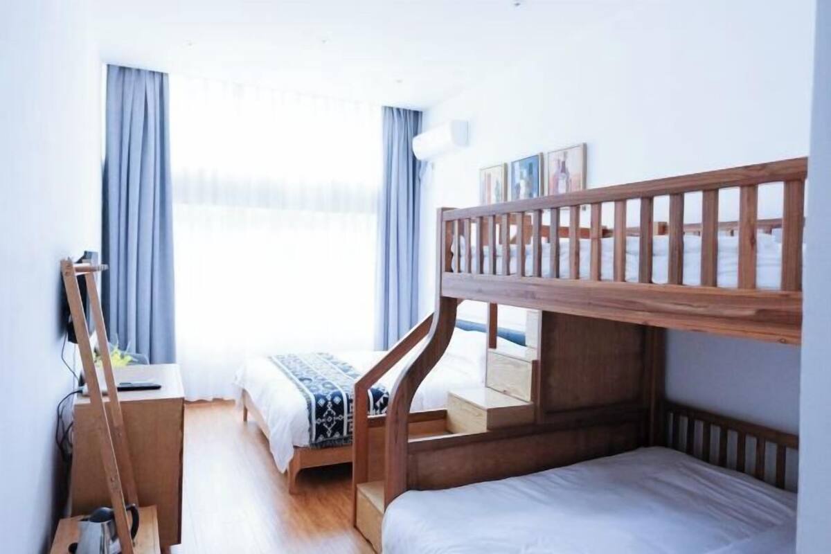 A room with bunk beds, a desk, and a window with curtains.