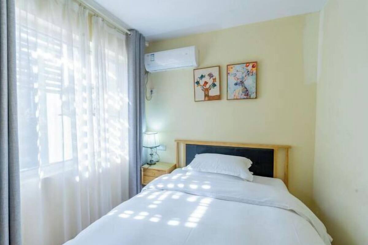 A hotel room with a bed, a nightstand, an air conditioner, and two wall-mounted paintings.