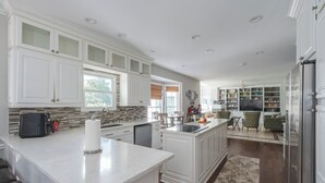 A spacious kitchen with white cabinetry, a central island, and a dining area with a TV. - Spacious 5-bedroom farmhouse in peaceful Nokesville with Pool (Nokesville)