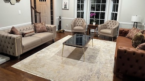 A living room with a beige sofa, two armchairs, a glass coffee table, and a large window with curtains. - Spacious 5-bedroom farmhouse in peaceful Nokesville with Pool (Nokesville)