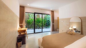 A modern hotel room with a large bed, a desk with a chair, a small trash bin, and a sliding glass door leading to a balcony with plants. - Nooju Pererenan (Pererenan)
