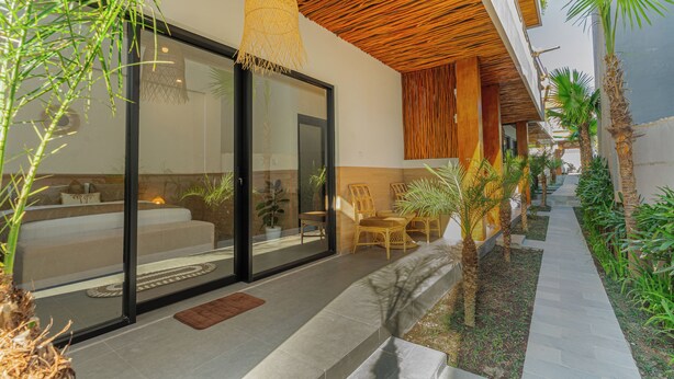 A modern outdoor seating area with a glass door entrance, a woven ceiling light, and a pathway lined with plants. - Nooju Pererenan (Pererenan)