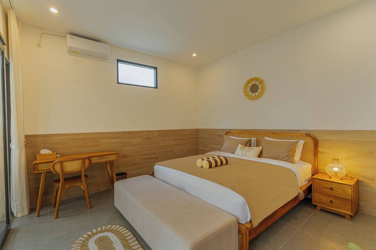 Une chambre à coucher comprenant un lit, une table de chevet, une commode, un bureau, une chaise et un appareil de climatisation.