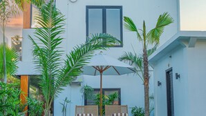 A modern building with a swimming pool, surrounded by tropical plants and two wooden chairs. - Nooju Pererenan (Pererenan)