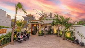 A courtyard with a traditional building, palm trees, and parked motorcycles. - Nooju Pererenan (Pererenan)