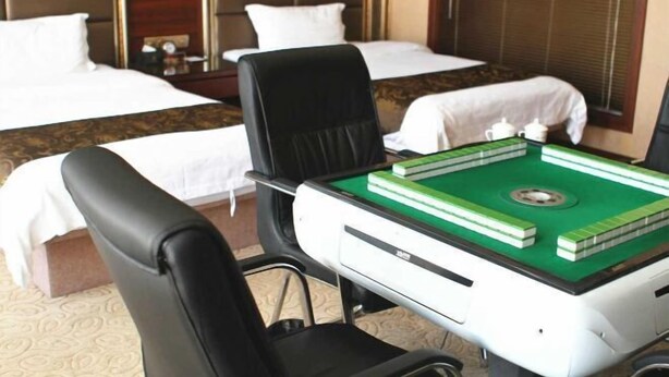 A hotel room with two beds, a desk with a green and white board game, and a black chair. - Royal Hotel (Tuquan)