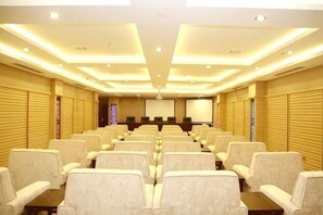 A conference room with rows of chairs, a projection screen, and a podium. - Royal Hotel (Tuquan)