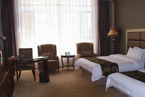 A hotel room with two beds, a desk, a chair, a small table, and a lamp. - Royal Hotel (Tuquan)