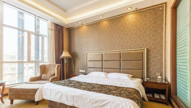 A hotel room with a large bed, a chair, a nightstand, and a window with a view of buildings. - Royal Hotel (Tuquan)