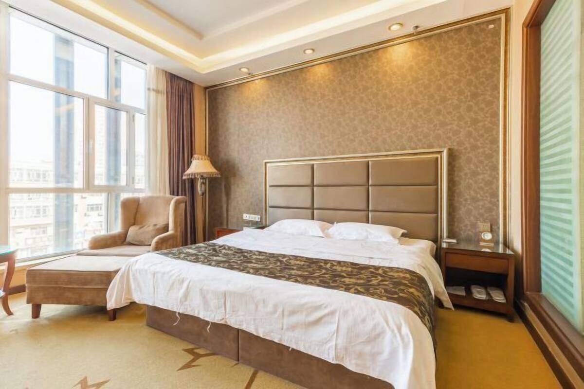 A hotel room with a large bed, a chair, a nightstand, and a window with a view of buildings.