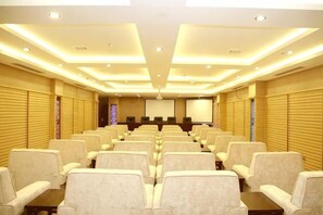 A conference room with rows of chairs, a projector screen, and a presentation area. - Royal Hotel (Tuquan)