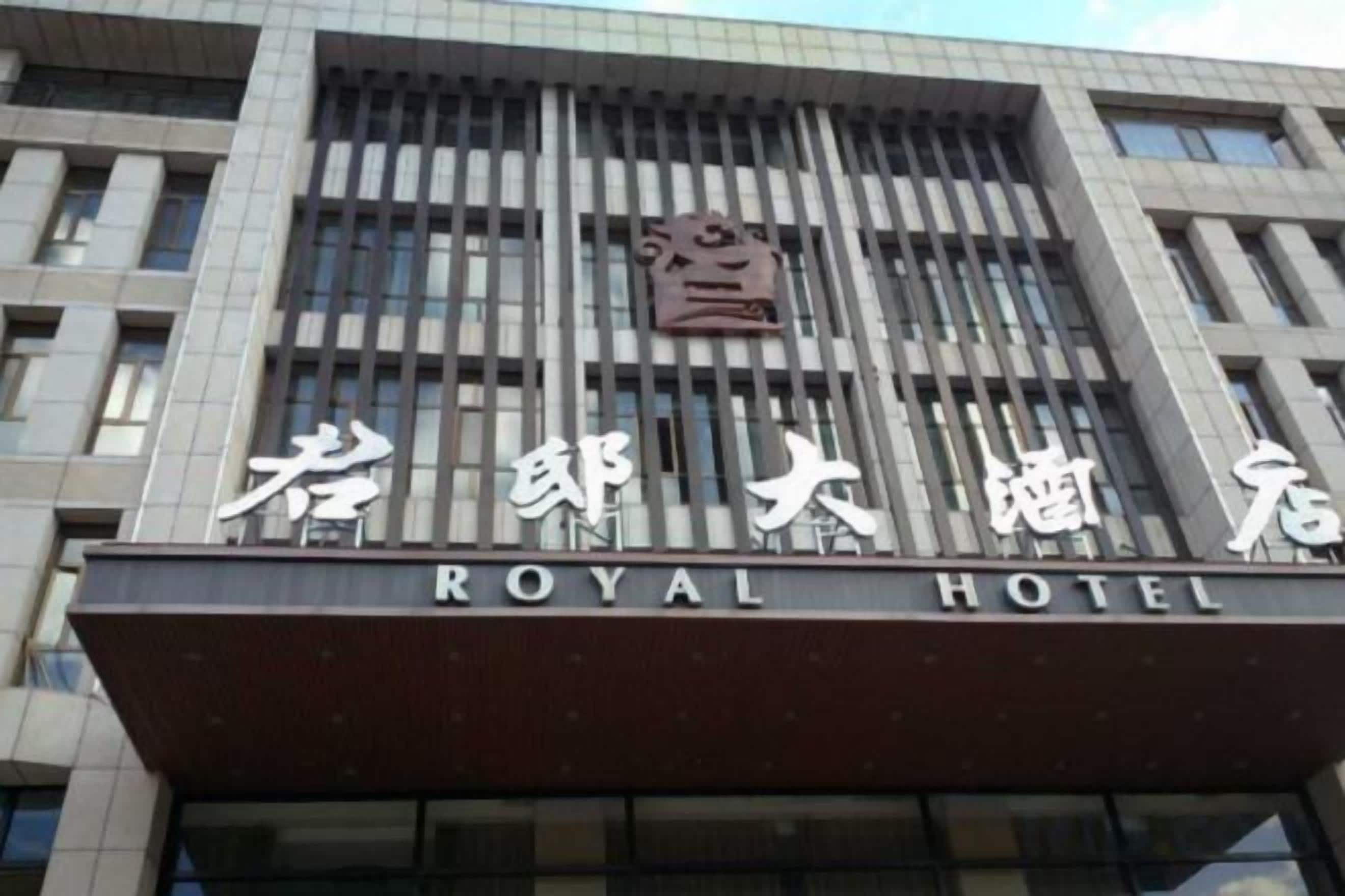 A hotel with a modern facade, featuring a prominent sign with the name 'ROYAL HOTEL' in English and Chinese characters.