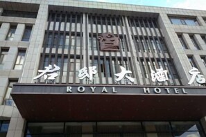 Un hotel con una fachada moderna, que presenta un cartel llamativo con el nombre 'ROYAL HOTEL' en inglés y caracteres chinos.